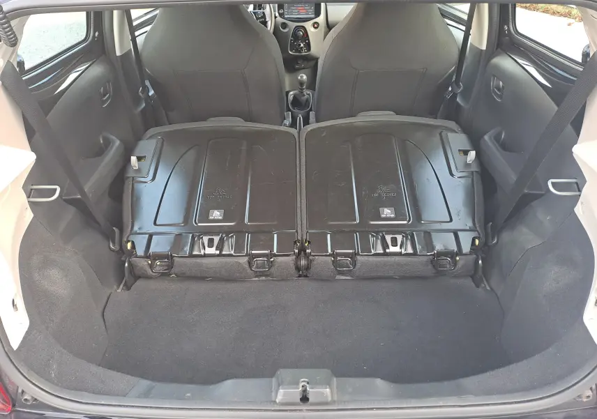 Coffre ouvert d'une Peugeot 108 noire, banquettes arrière rabattues vues de l'arrière offrant un espace de chargement plat.
