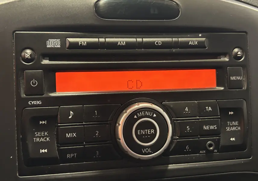Gros plan sur la radio CD du tableau de bord du Nissan Juke noir métal, affichage rouge et boutons de commande visibles.