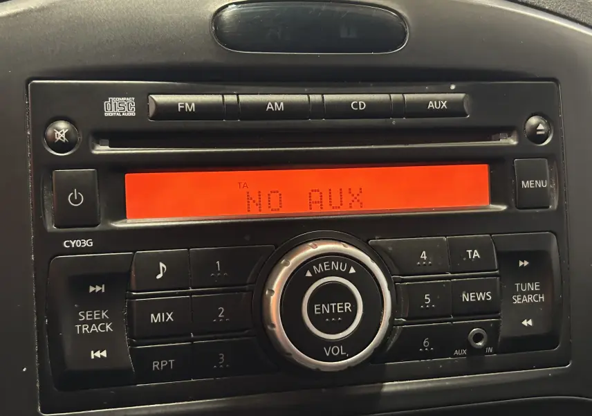 Gros plan sur la radio d’origine du Nissan Juke 2012 avec écran orange affichant "NO AUX" et boutons noirs.
