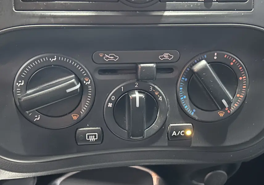 Vue rapprochée des commandes de climatisation du Nissan Juke noir métal, avec bouton A/C allumé et réglages manuels visibles.