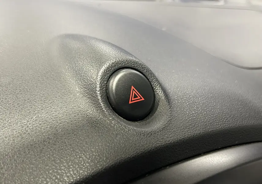 Gros plan sur le bouton de warning noir avec symbole rouge sur le tableau de bord d’un Nissan Juke noir métal.