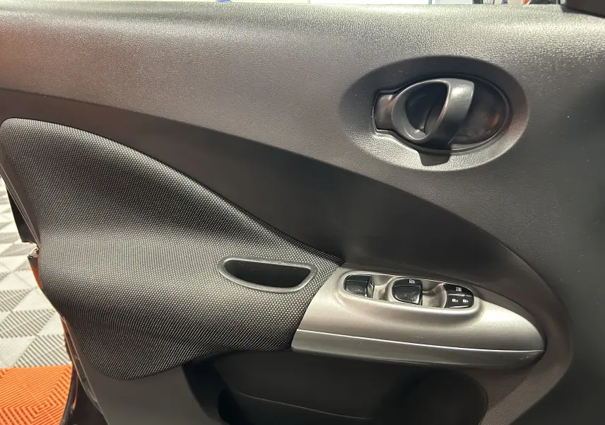 Vue rapprochée de la porte avant gauche du Nissan Juke noir métal, avec commandes de vitres et poignée intérieure.