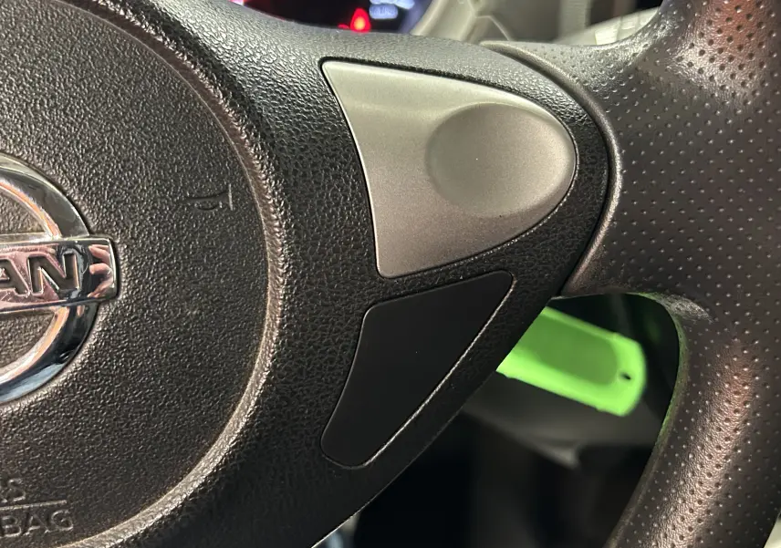 Gros plan sur le volant noir perforé du Nissan Juke 2012 avec logo chromé et commandes intégrées côté droit.