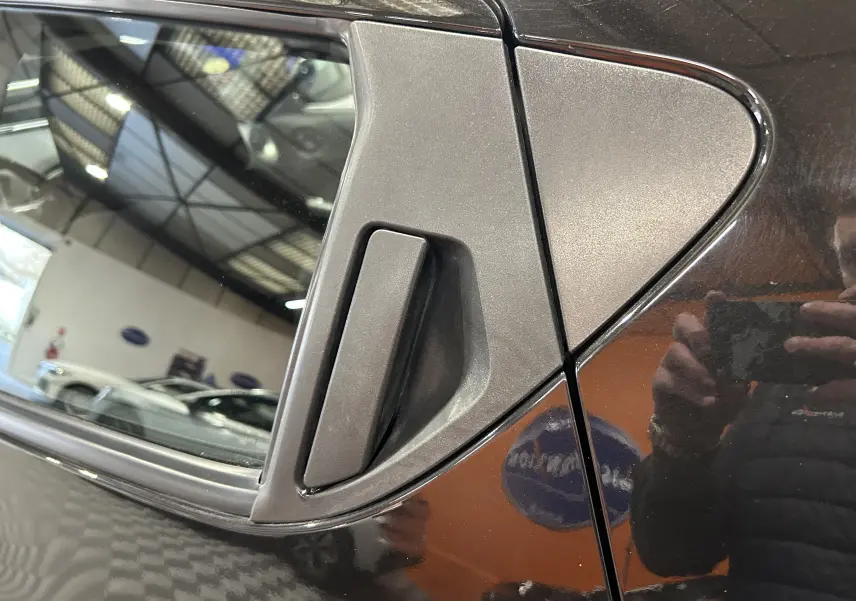 Gros plan sur la poignée de porte arrière côté droit d’un Nissan Juke noir métal 2012 avec reflet intérieur visible.