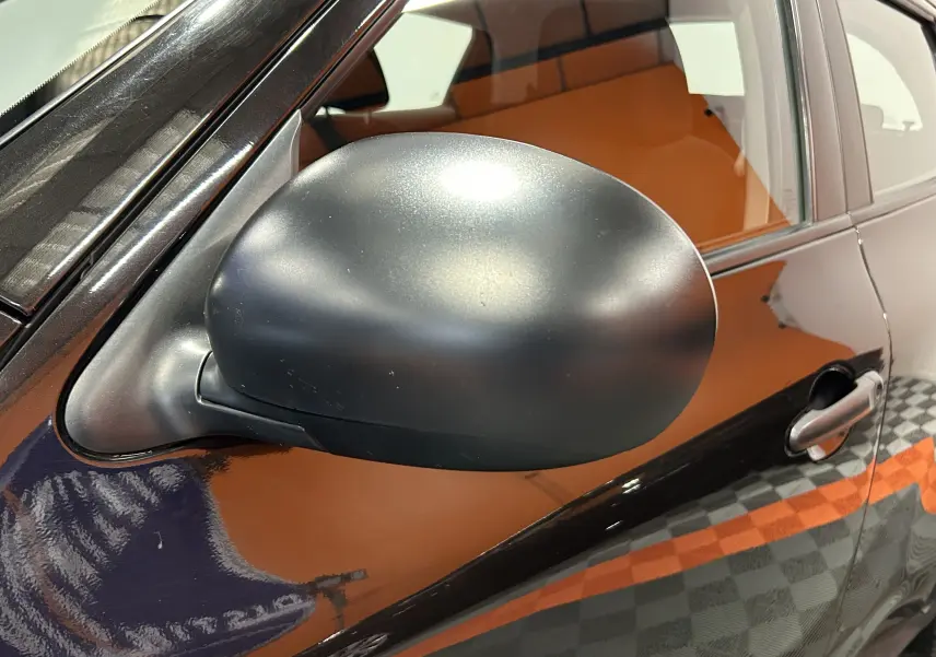 Gros plan sur le rétroviseur côté gauche d'un Nissan Juke noir métal avec poignée de porte visible.