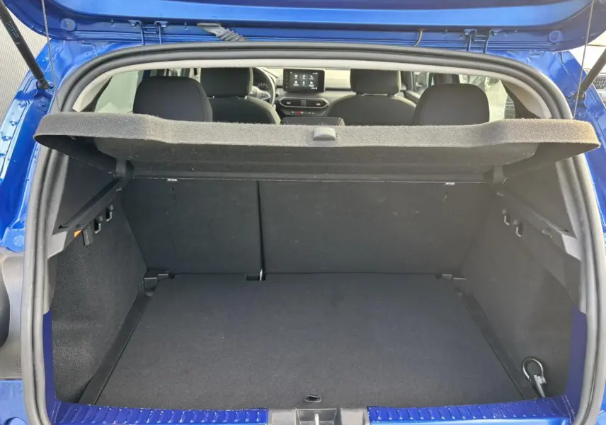 Coffre ouvert vu de l'arrière d'une Dacia Sandero Stepway Bleu Iron, intérieur noir et tablette de coffre relevée.