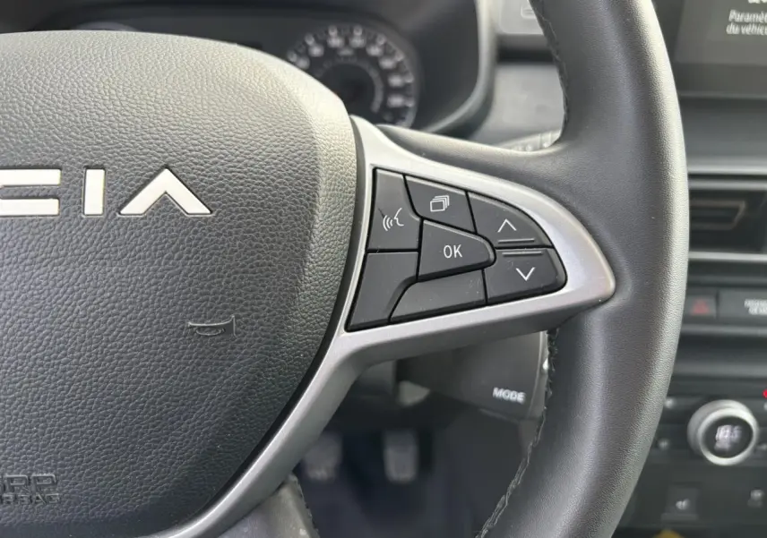 Gros plan sur le volant noir du Dacia Sandero Stepway 2025, avec commandes multifonctions à droite et logo central.