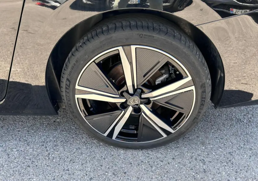 Gros plan sur la jante alliage 18 pouces noire et argentée du côté gauche d'une Peugeot 308 SW PHEV 225 e-EAT8 GT noire.
