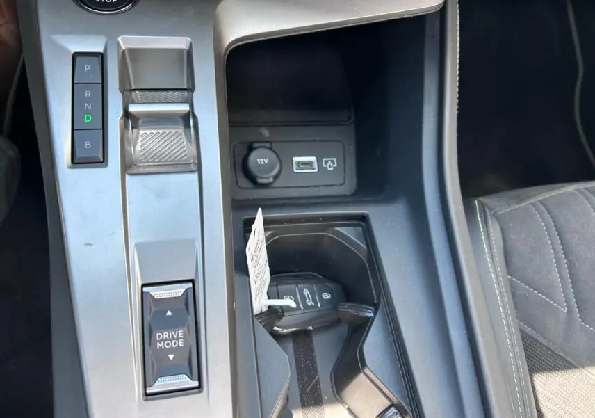 Vue rapprochée de la console centrale de la Peugeot 308 SW PHEV 225 GT 2023, avec clé, levier de vitesses et ports USB visibles.