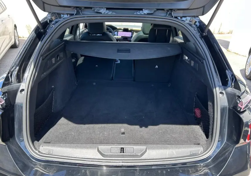 Coffre ouvert vu de l'arrière d'une Peugeot 308 SW PHEV noire, avec banquette arrière rabattable et cache-bagages.