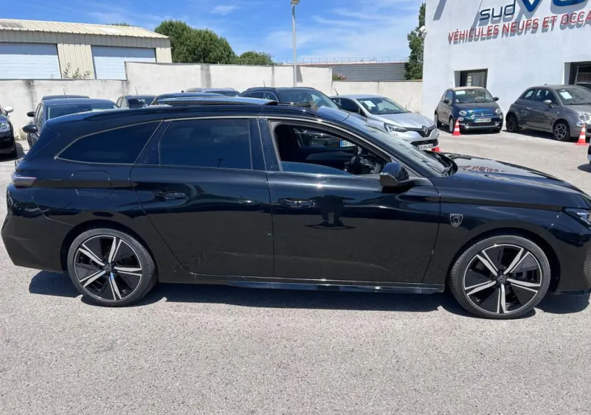 Profil côté gauche d'une Peugeot 308 SW PHEV 225 e-EAT8 GT noire avec jantes alliage 18 pouces et barres de toit.