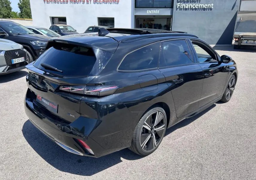Peugeot 308 SW PHEV noir vue 3/4 arrière droit, jantes alliage 18 pouces, vitres teintées et barres de toit visibles.