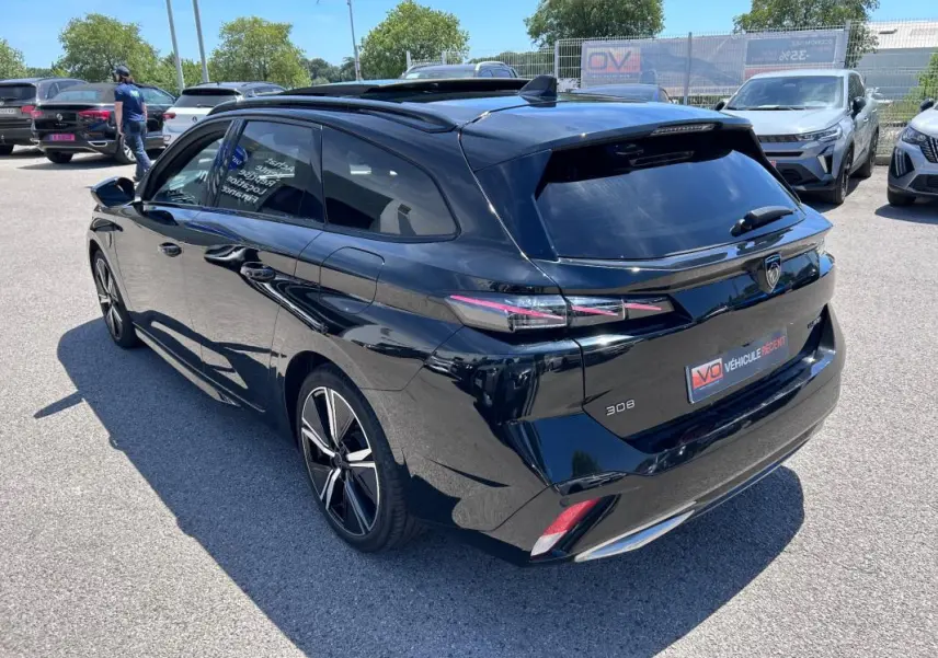 Vue 3/4 arrière droite d'une Peugeot 308 SW PHEV noire 2023 avec jantes alliage 18 pouces et toit ouvrant électrique.