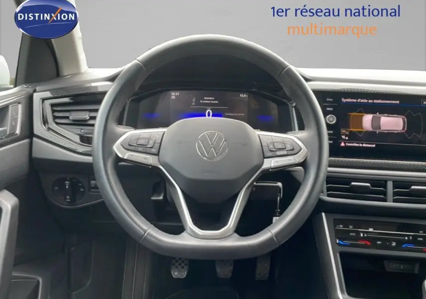 Vue intérieure centrée sur le volant cuir noir d'une Volkswagen Polo blanche de 2022 avec tableau de bord digital et écran tactile.