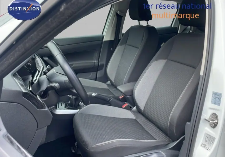 Vue intérieure côté conducteur de la Volkswagen Polo blanche 2022, mettant en valeur les sièges tissu gris et la boîte manuelle.