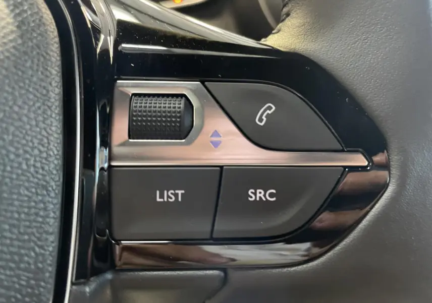 Gros plan sur les commandes multimédia noires intégrées au volant du Peugeot 2008 hybride blanc.