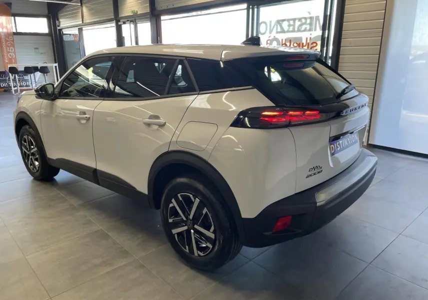 Peugeot 2008 blanc vue 3/4 arrière droit en intérieur, feux arrière LED allumés et jantes alliage noires.