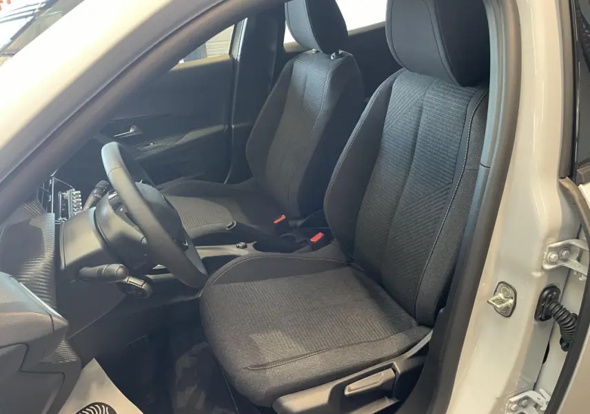 Vue intérieure côté conducteur du Peugeot 2008 blanc, mettant en valeur les sièges tissu gris et le volant compact noir.