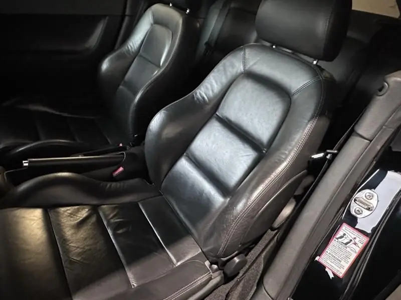 Gros plan sur les sièges avant en cuir noir de l'Audi TT Coupé 2002, mettant en valeur leur design sportif et l'intérieur sombre.