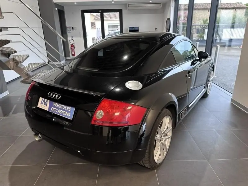 Audi TT Coupé noir 2002 vu en 3/4 arrière droit, avec jantes argentées et bouchon de réservoir alu visible.