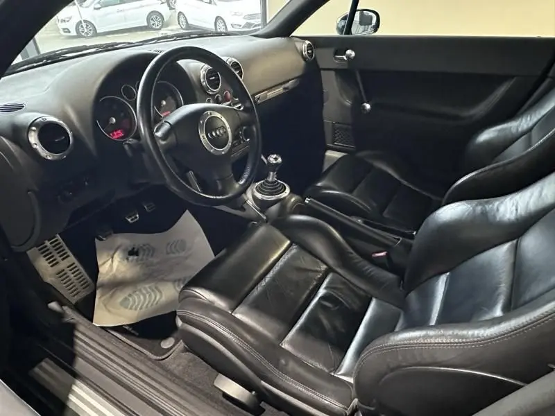 Intérieur noir cuir de l'Audi TT Coupé 180 cv 2002, vue côté conducteur avec volant et levier de vitesse manuelle visibles.