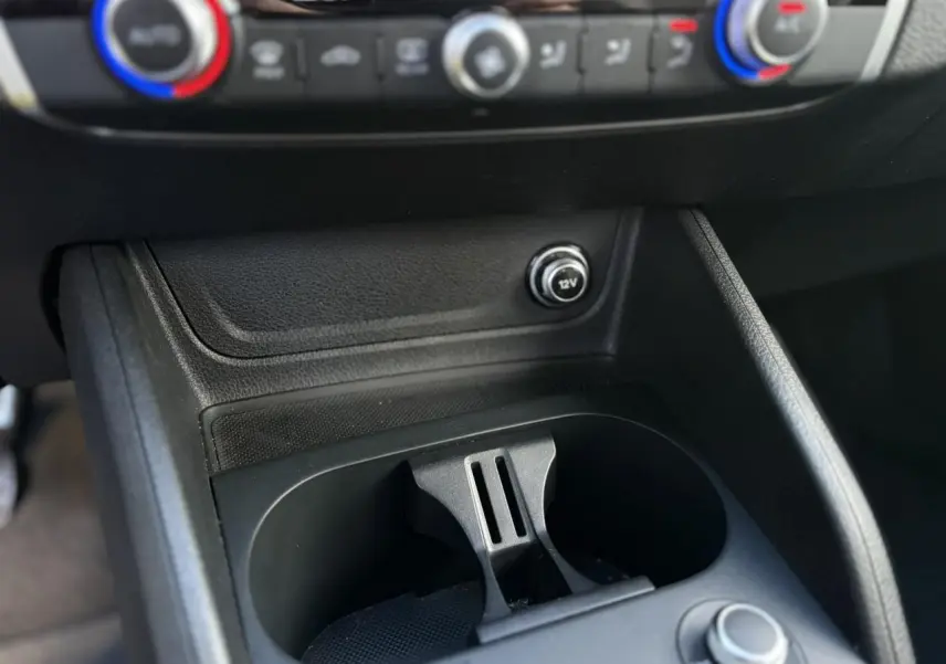 Gros plan sur la console centrale de l'Audi Q2 30 TDI S-Line 2025, montrant les porte-gobelets et prise 12V.