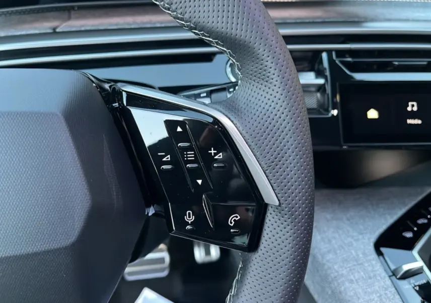 Gros plan sur le volant cuir perforé du Peugeot 5008 Hybrid 145 GT avec commandes multifonctions et tableau de bord numérique.