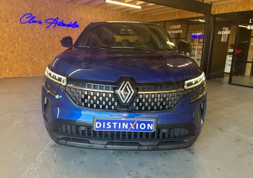 Vue de face d'un Renault Austral bleu 2024 avec calandre à damier et logo central, dans un showroom intérieur.