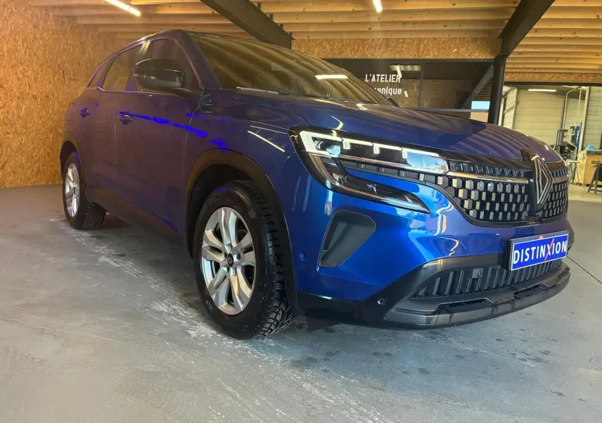 Renault Austral bleu en 3/4 avant droit dans un garage, mettant en valeur sa calandre et ses phares LED modernes.