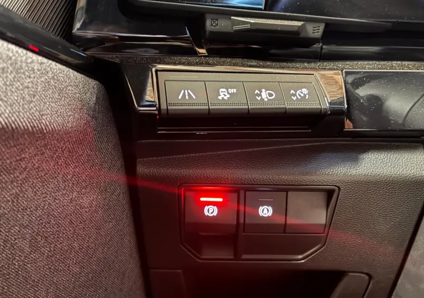 Gros plan sur les commandes du tableau de bord du Renault Austral bleu 2024, avec bouton de frein à main électronique allumé.