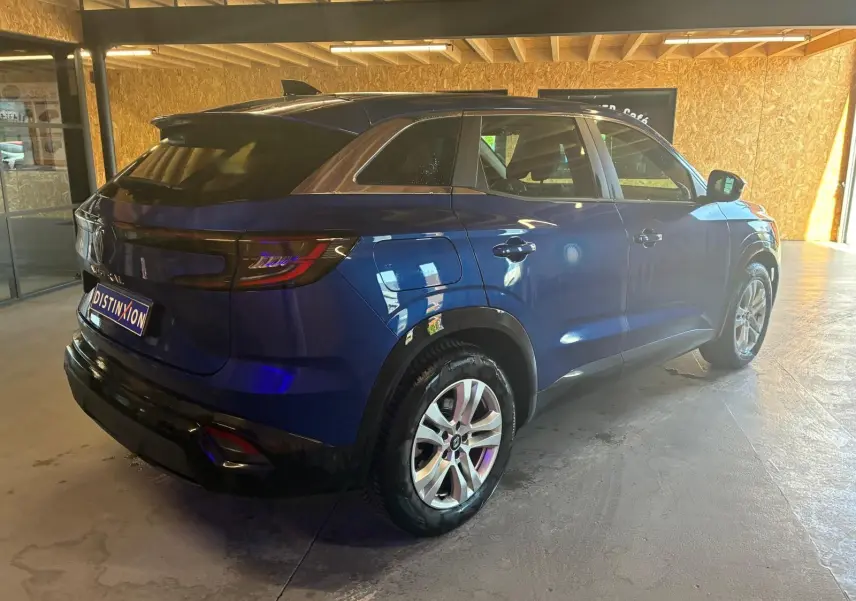 Vue 3/4 arrière droite d’un Renault Austral bleu 2024 dans un garage avec toit en bois, mettant en valeur ses feux arrière et jantes.
