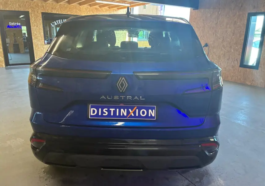 Vue arrière d'un Renault Austral bleu 2024 avec feux arrière étirés et plaque Distinxion visible en intérieur.