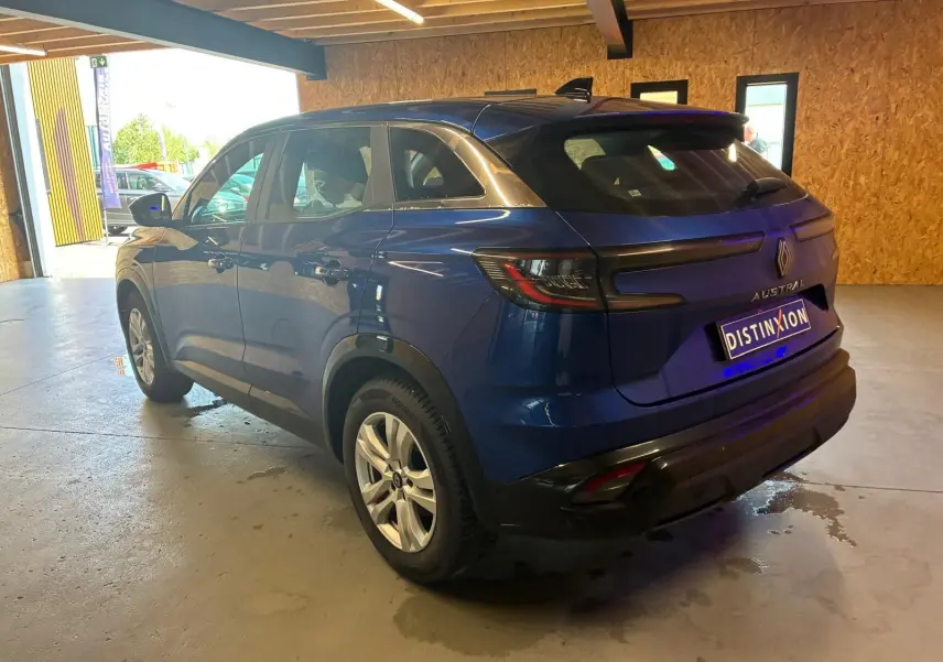 Vue 3/4 arrière droite d'un Renault Austral bleu 2024 avec feux arrière LED et toit noir dans un garage.