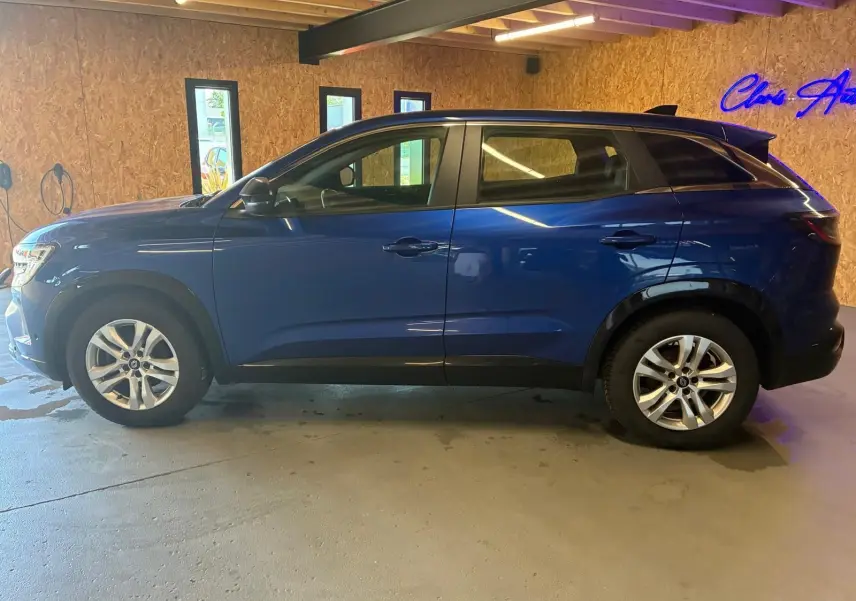 Profil droit d’un Renault Austral bleu 2024 stationné en intérieur, avec jantes argentées et toit noir contrastant.
