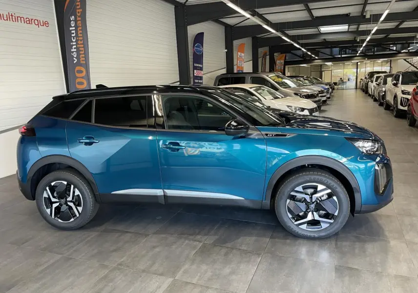 Vue de profil côté gauche d’un Peugeot 2008 bleu hybride 2026 avec jantes distinctives et toit noir en concession.