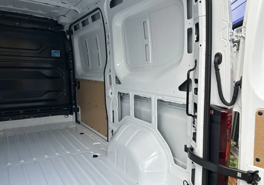 Vue intérieure arrière du fourgon Renault Master blanc, montrant l’espace de chargement vide avec parois métalliques et panneau bois.