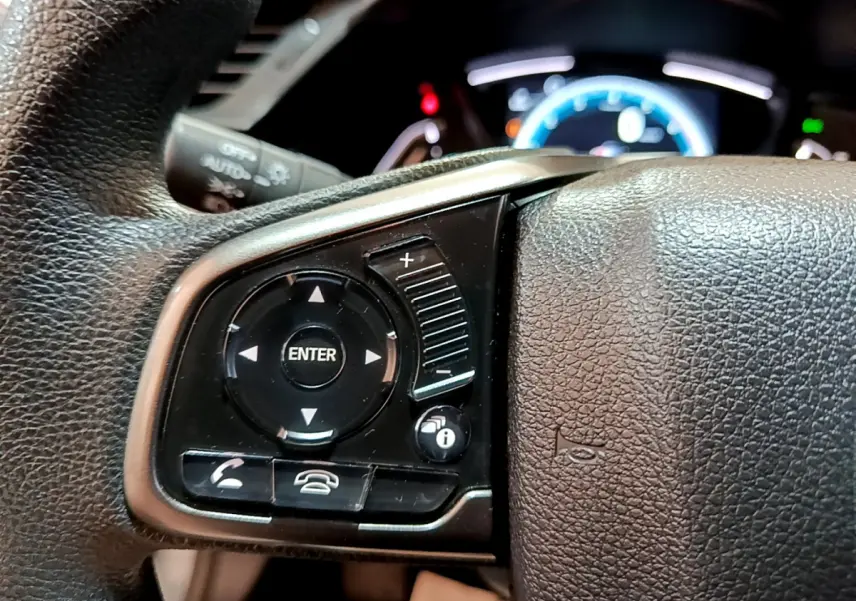 Gros plan sur les commandes du volant cuir côté gauche de la Honda Civic 2020 gris foncé avec tableau de bord éclairé.