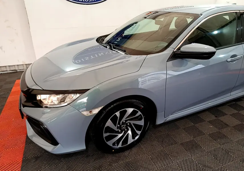 Vue 3/4 avant droit d'une Honda Civic gris clair avec jantes alliage et phares allumés en intérieur showroom.