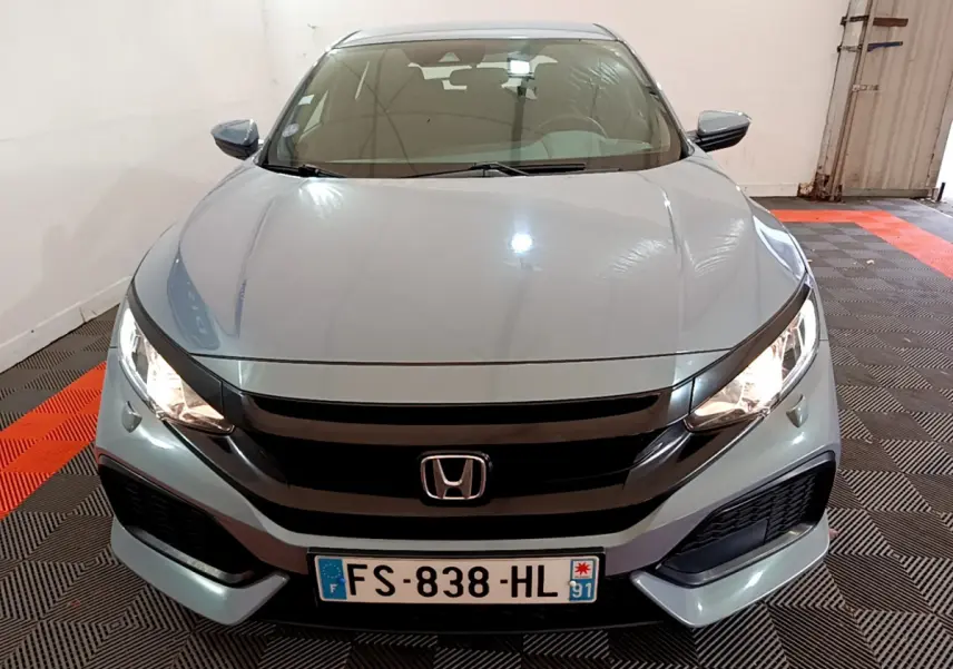 Vue frontale d'une Honda Civic 1.0 i-VTEC Exclusive gris foncé avec phares allumés en intérieur.