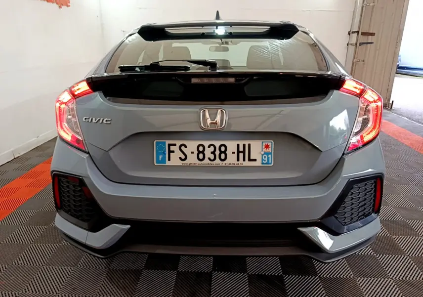 Vue arrière d'une Honda Civic gris foncé 2020 avec feux arrière allumés et aileron noir.