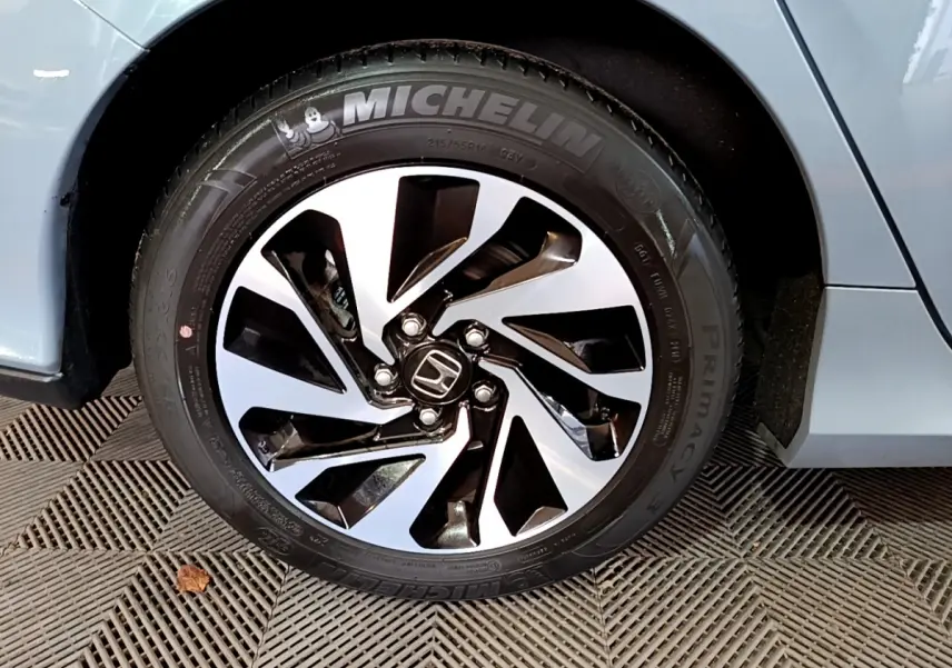 Gros plan sur la roue avant droite d'une Honda Civic gris foncé avec jante alliage noire et argentée.