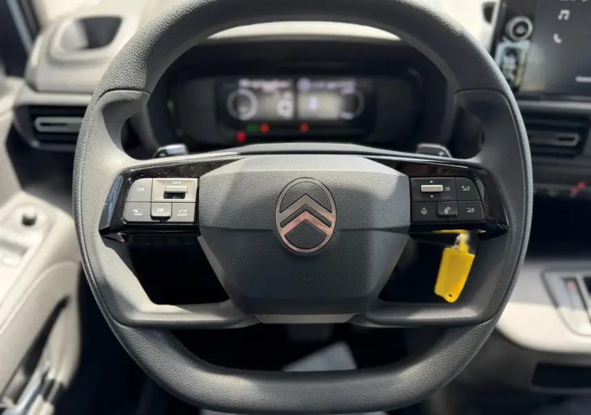 Gros plan sur le volant multifonction noir du Citroën Berlingo ë-136 2025 avec commandes intégrées et logo central rosé.