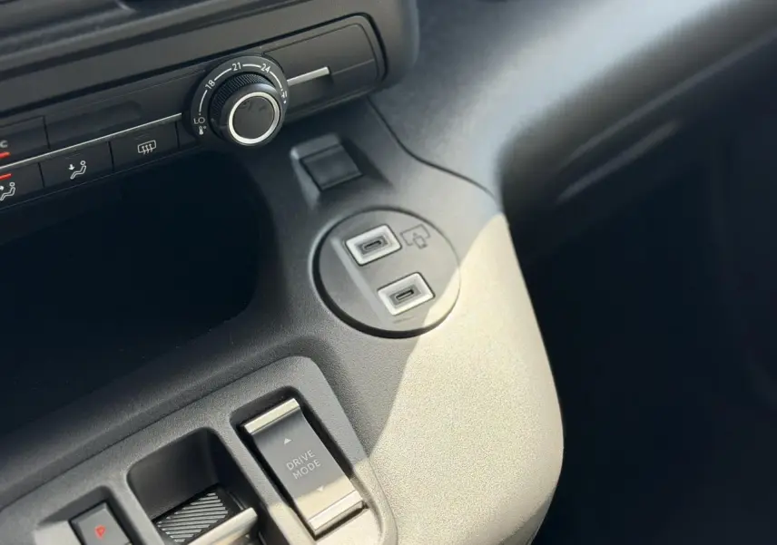 Gros plan sur la console centrale grise du Citroën Berlingo ë-136, montrant le bouton Drive Mode et ports USB.