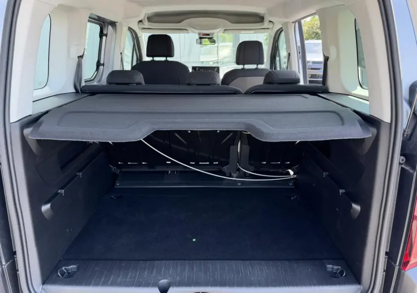 Coffre ouvert d’un Citroën Berlingo ë-136 gris Artense, vue arrière montrant la tablette cache-bagages et les sièges noirs.