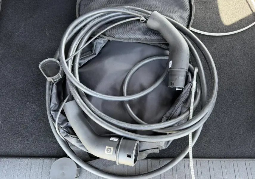 Câble de recharge électrique noir enroulé dans le coffre d’un Citroën Berlingo gris Artense, vue de dessus.