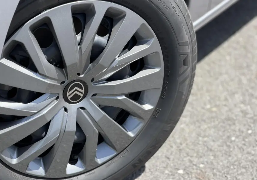 Gros plan sur la jante tôlée grise avec enjoliveur pleine roue et logo Citroën au centre, sur route asphaltée.