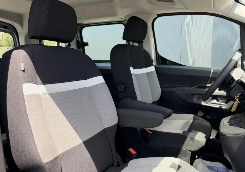 Vue intérieure côté conducteur du Citroën Berlingo 2025, sièges tissu bicolore gris et noir avec accoudoirs.