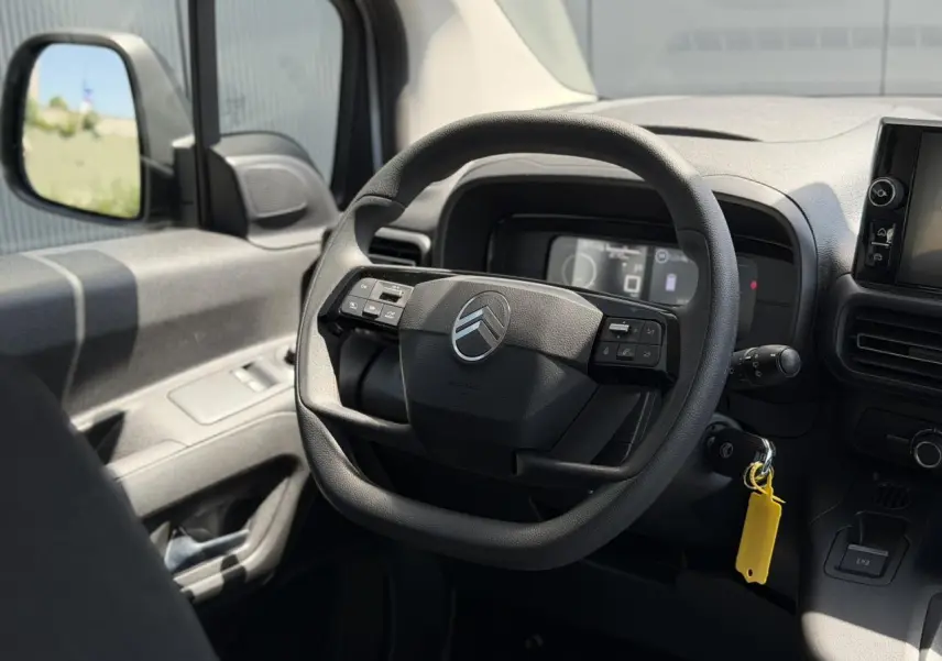 Vue intérieure centrée sur le volant multifonction du Citroën Berlingo ë-136 gris Artense, tableau de bord et rétro gauche visibles.