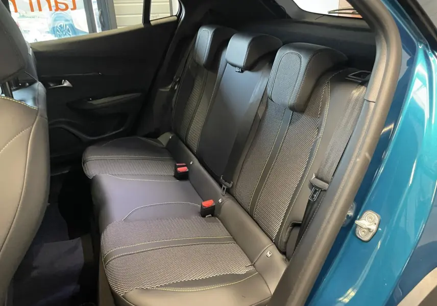 Vue intérieure côté gauche sur la banquette arrière en tissu et cuir noir avec surpiqûres vertes d’un Peugeot 2008 bleu.