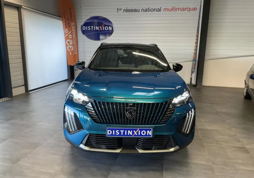 Vue frontale d'un Peugeot 2008 bleu métallisé avec calandre noire et feux LED 3 griffes allumés en showroom.